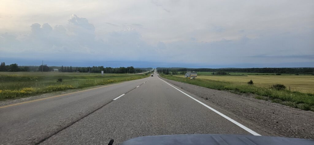 A photo from the front seat of a vehicle heading down an open country road during summer