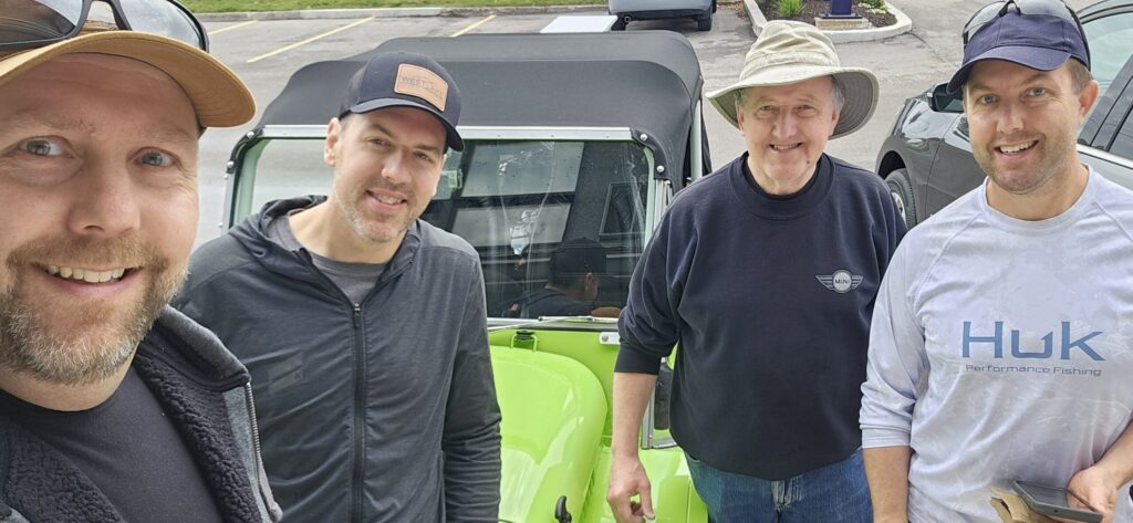 Four men standing in front of a Mini Moke