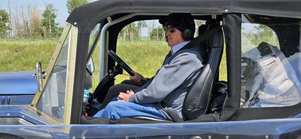A man is sitting in the passenger seat of a Blue Mini Moke as it drives down the road