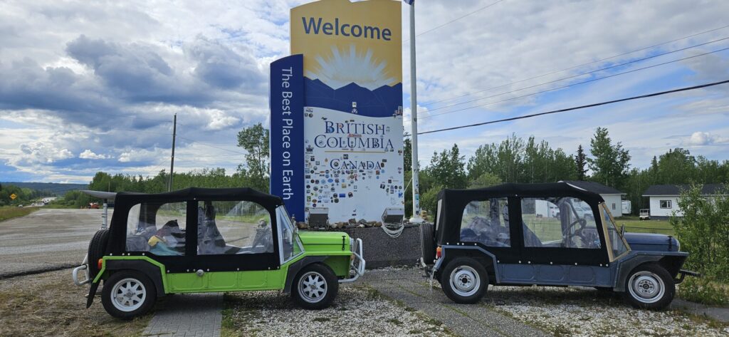 Two Mini Mokes next to the "Welcome to British Columbia" sign