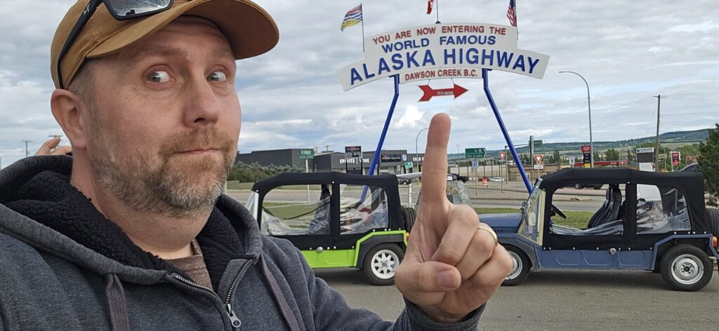 A man pointing at the Alaskan Highway sign in Dawson Creek