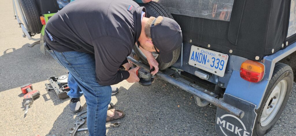 A man working on the trailer hitch on a Mini Moke