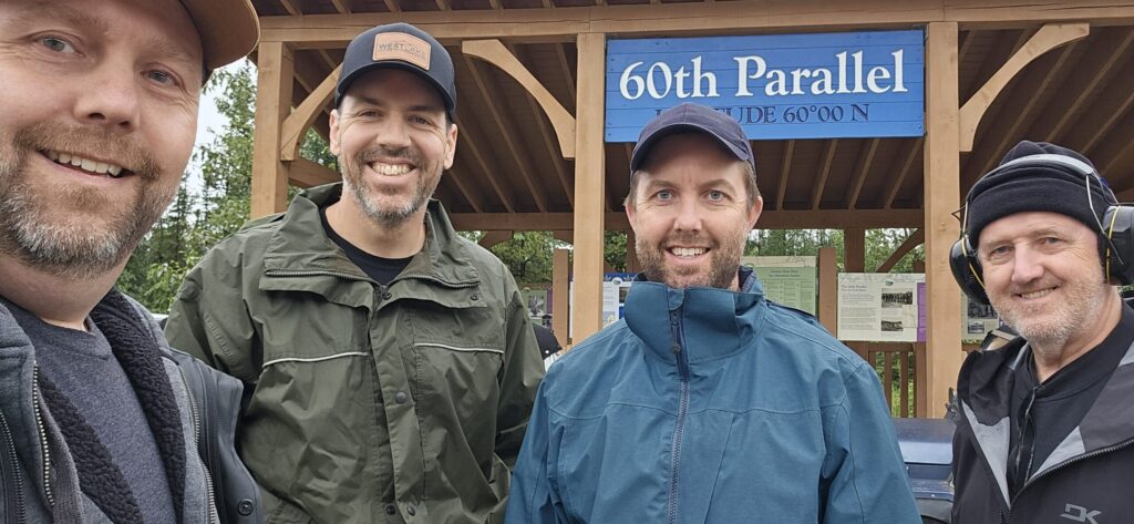 4 men standing near the 60th Parallel sign in the Yukon Territory