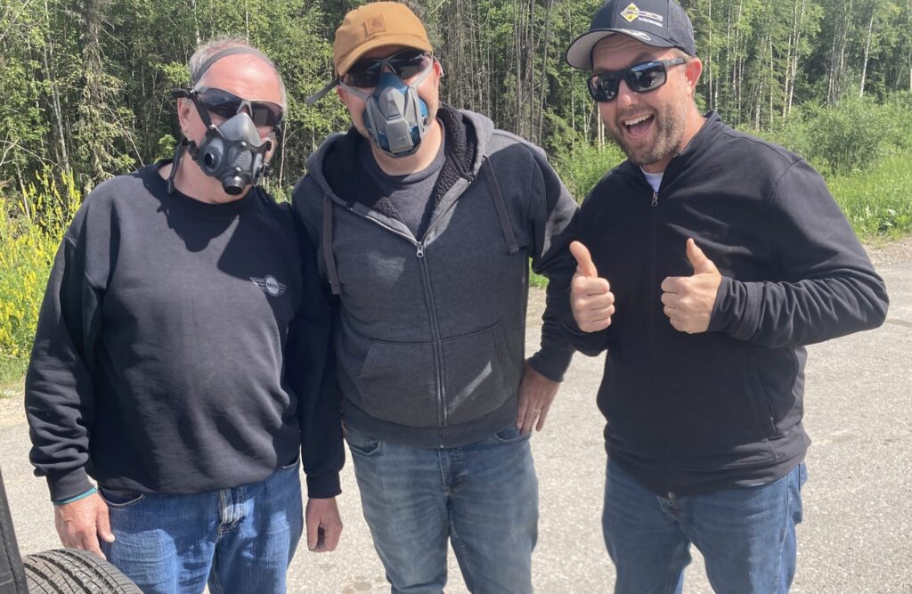 Three guys standing together. All wearing sunglasses and two wearing breathing masks.